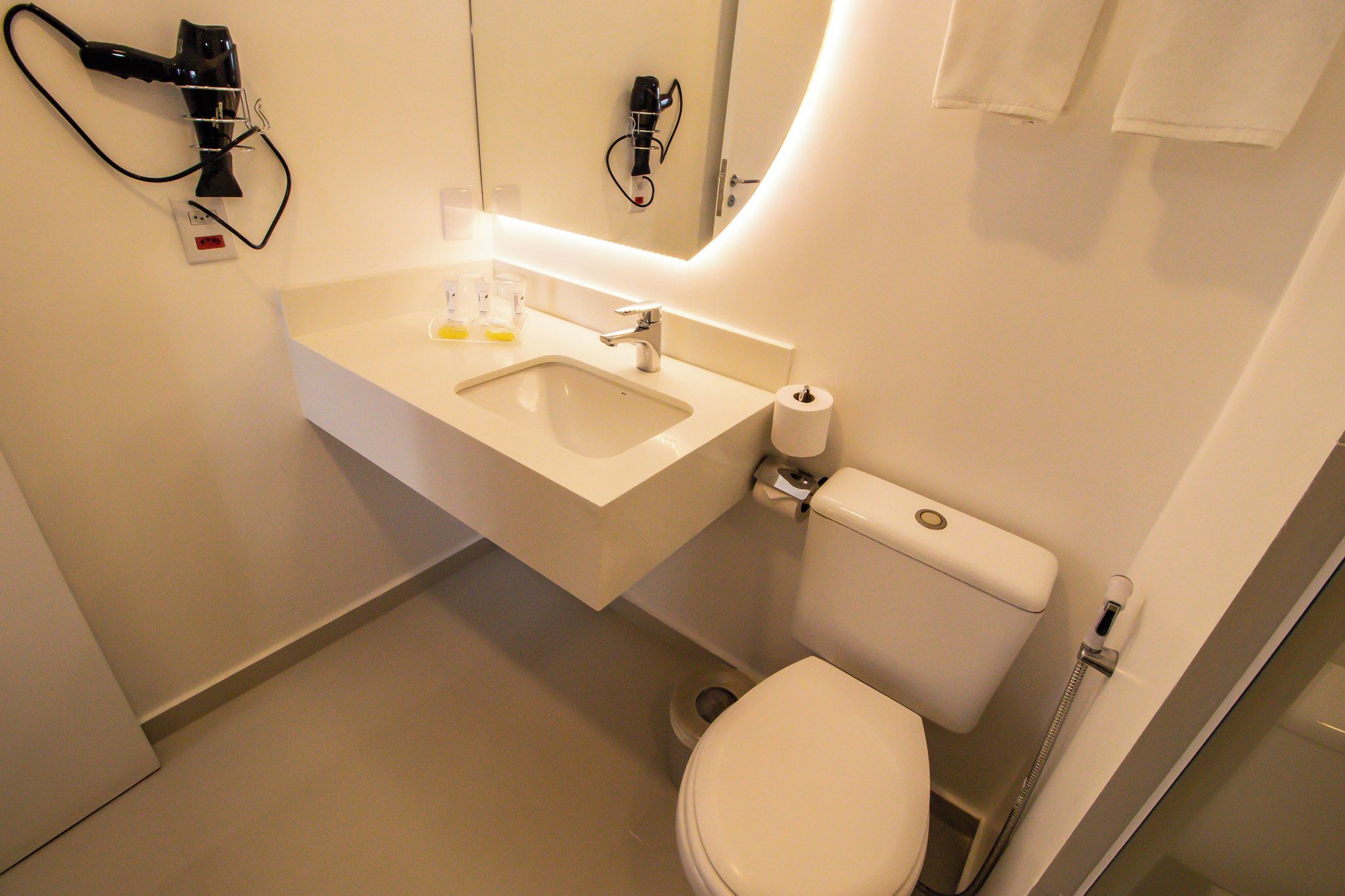 Un baño moderno con lavamanos, espejo y retrete blancos.