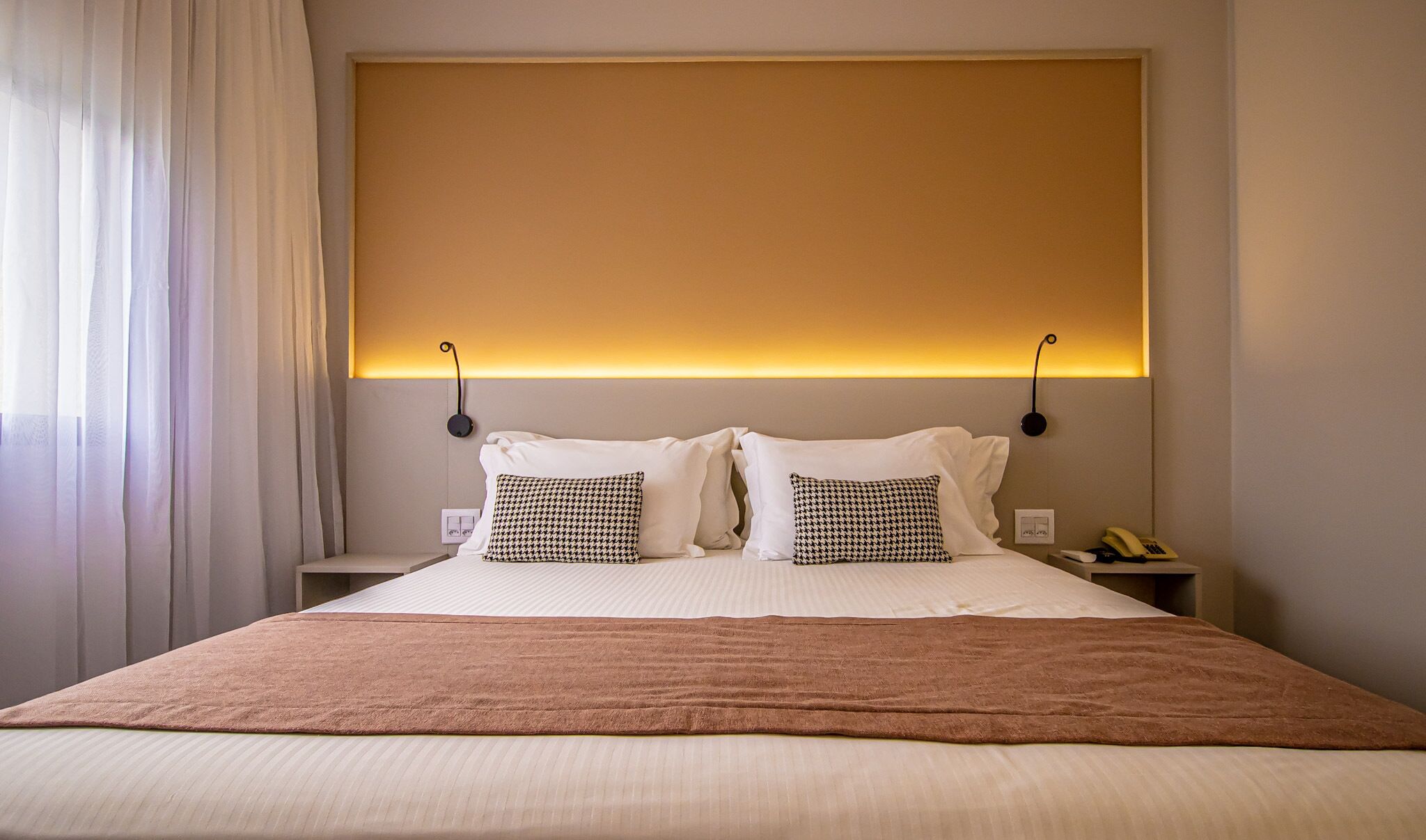 A hotel room with a large bed, two bedside tables, a nightstand, and a wall-mounted lamp.