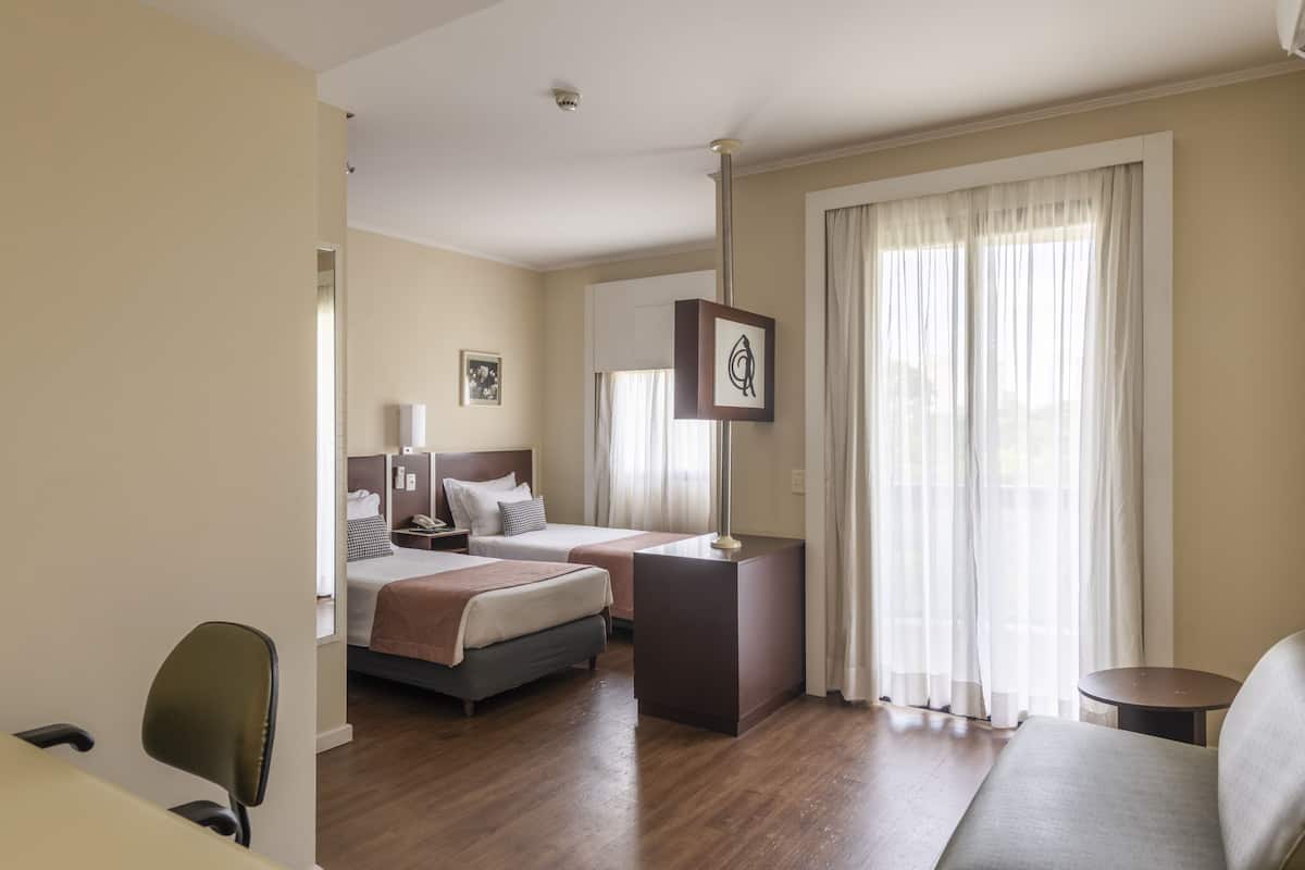 A hotel room with a bed, bedside tables, a desk, a chair, and a sofa.