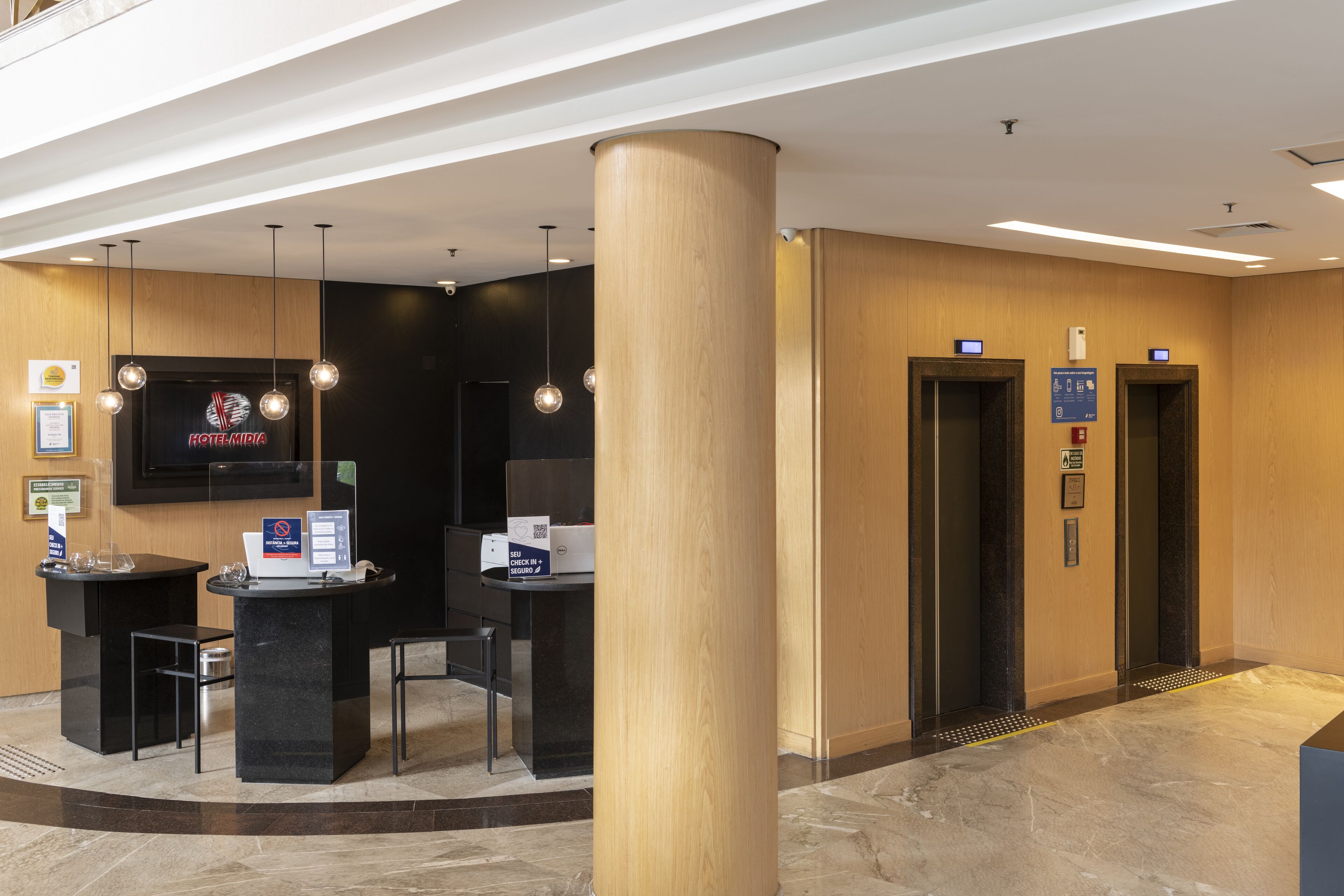 Un espace d’accueil d’hôtel comprenant un comptoir de réception, un écran de télévision et deux ascenseurs.