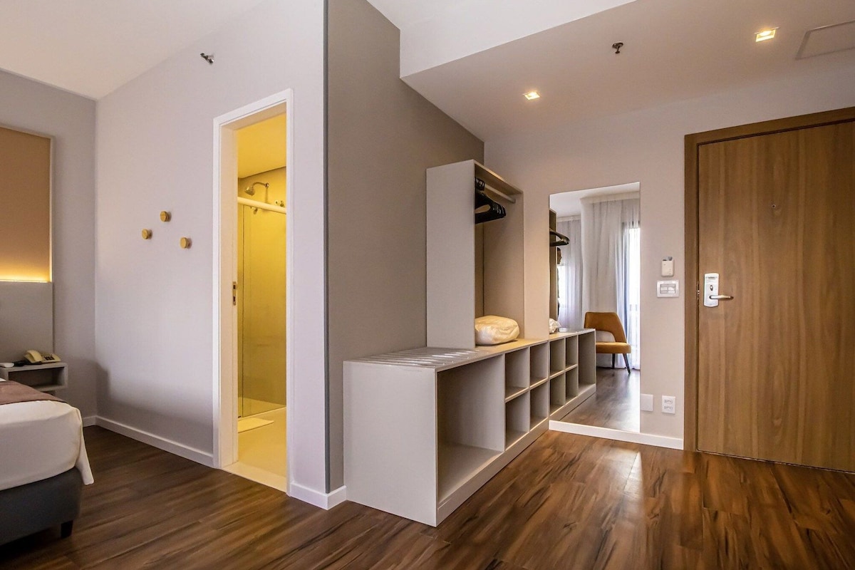 A hotel room with a wooden floor, a bed, a wardrobe, and a seating area.