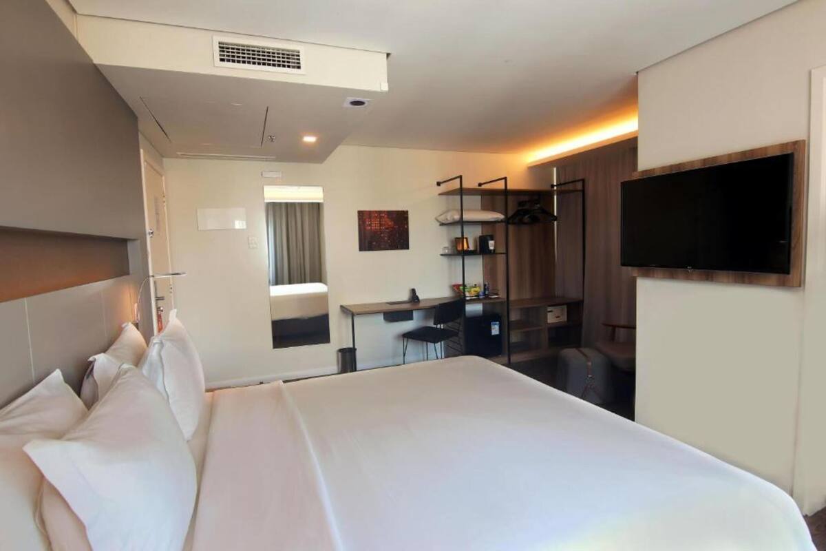 Une chambre d’hôtel avec un grand lit, un bureau, une chaise, un téléviseur fixé au mur et une fenêtre.