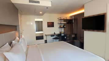 Quarto de hotel com uma cama grande, uma escrivaninha, uma cadeira, uma TV na parede e uma janela.
