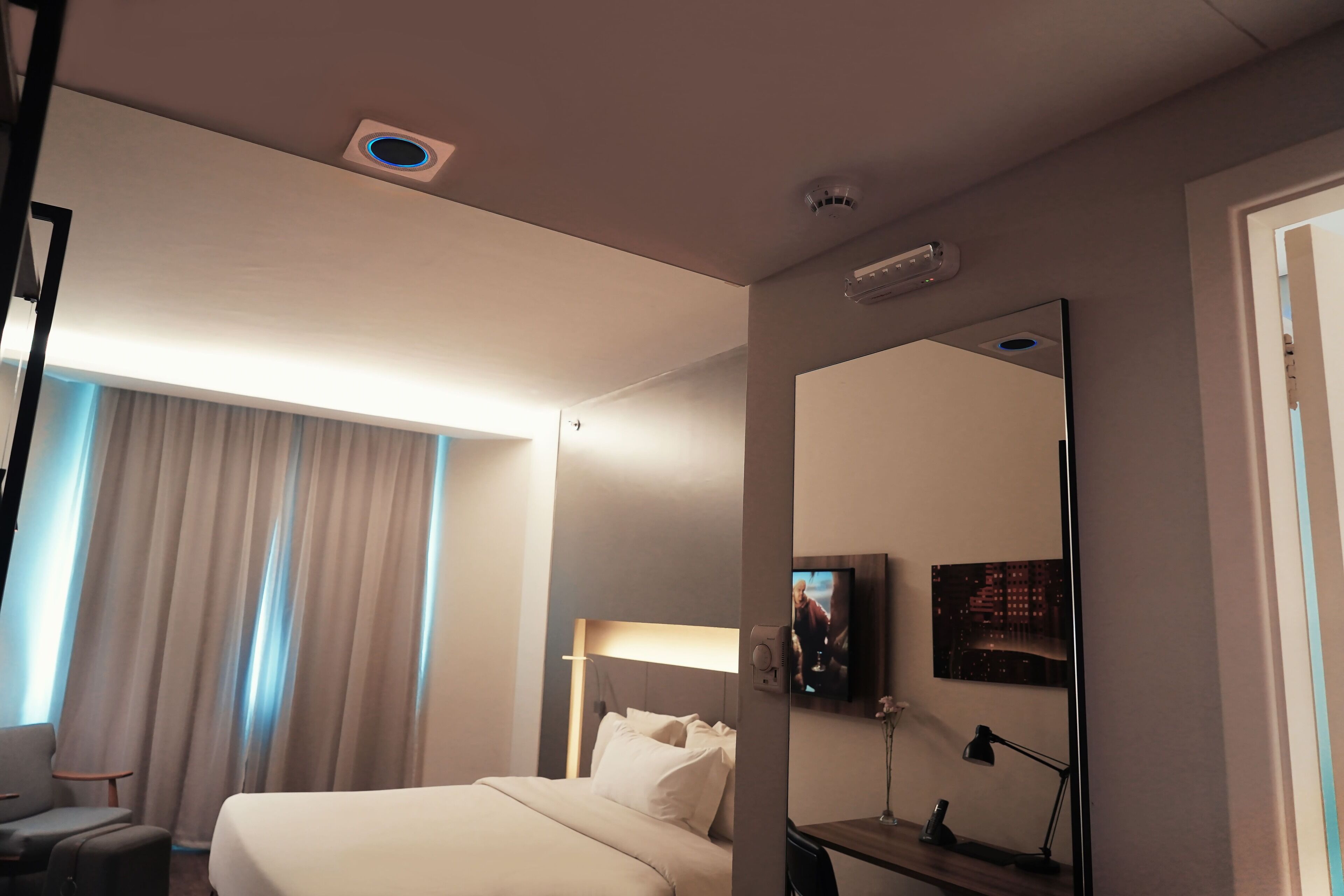 Hotellihuone, jossa on sänky, työpöytä, tuoli, televisio ja suuri peili.