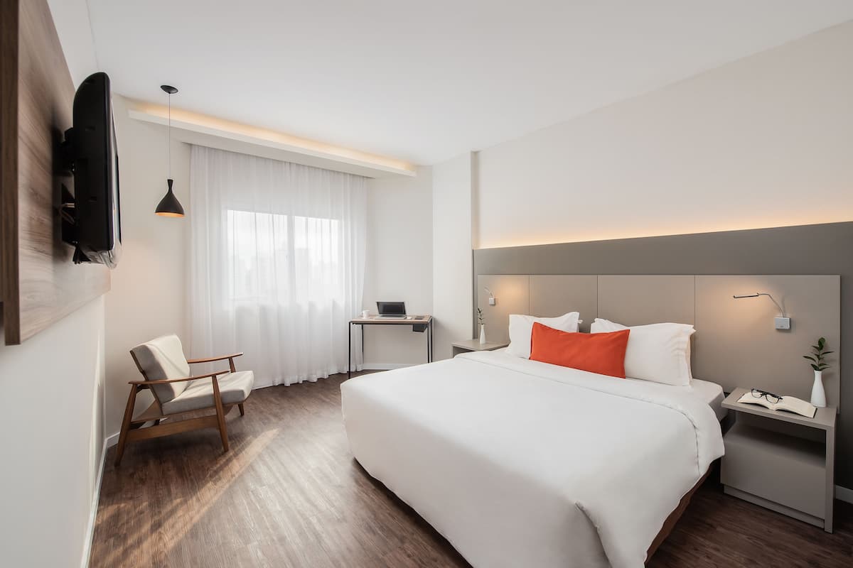 Une chambre d’hôtel moderne équipée d’un grand lit, d’un bureau, d’une chaise et d’un téléviseur fixé au mur.