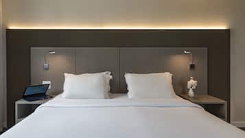 Un lit bien fait, avec du linge de lit blanc, deux tables de chevet avec des lampes, un ordinateur portable et un vase rempli de fleurs posé sur l’une des tables.