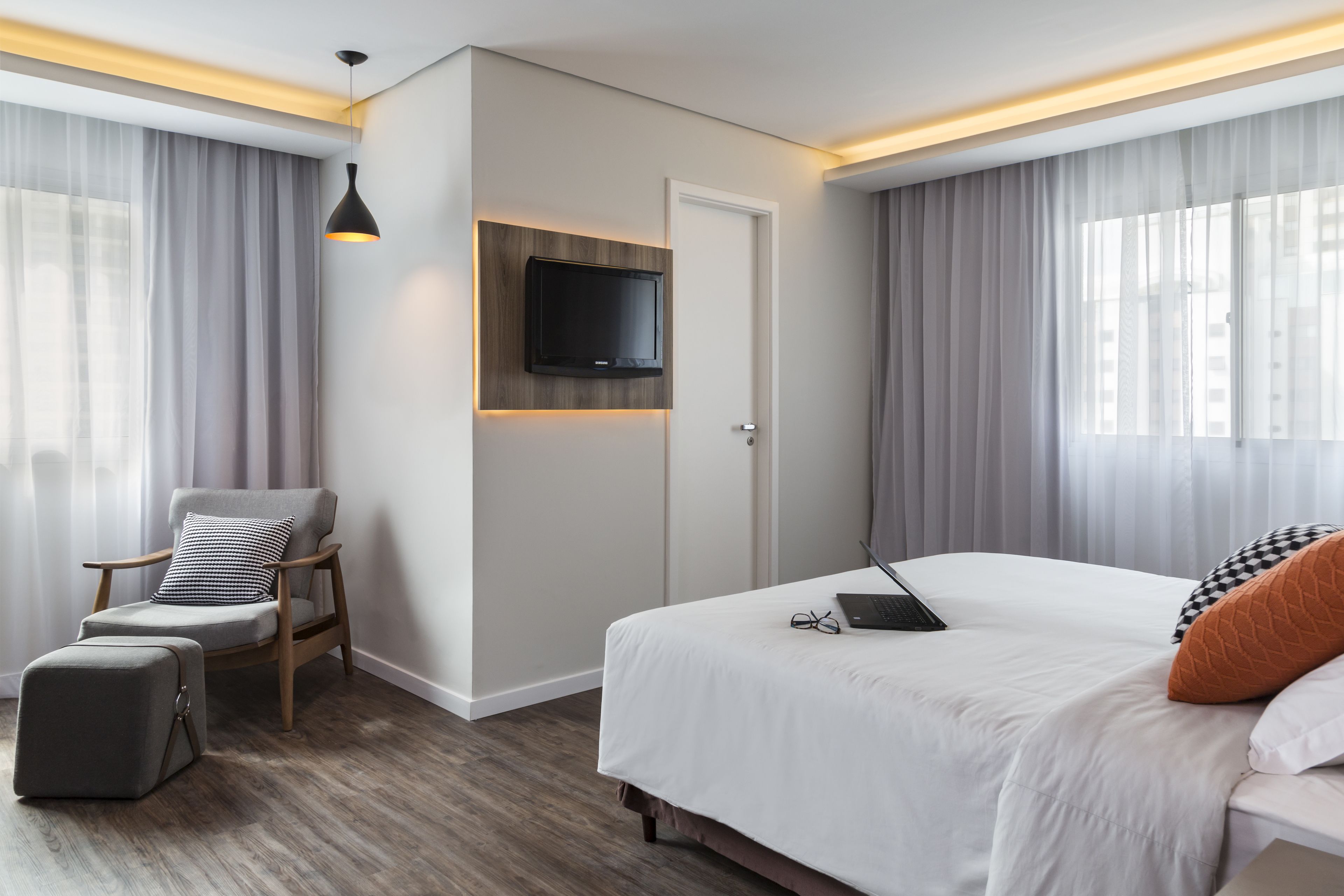 Ett modernt hotellrum med en säng, ett skrivbord med en bärbar dator, en stol och en tv som är monterad på väggen.