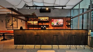 Eine moderne Bar mit einer Holztresen, Barhocker und einem großen Bildschirm, der ein Essenszene zeigt.