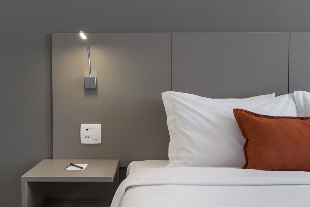 Une chambre d’hôtel moderne avec un lit bien fait, une table de chevet avec une lampe et une prise de courant.