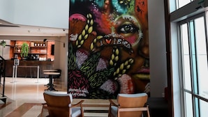 Un hall d’entrée agrémenté d’une grande fresque colorée, d’un lustre moderne et d’un espace détente avec des sièges.