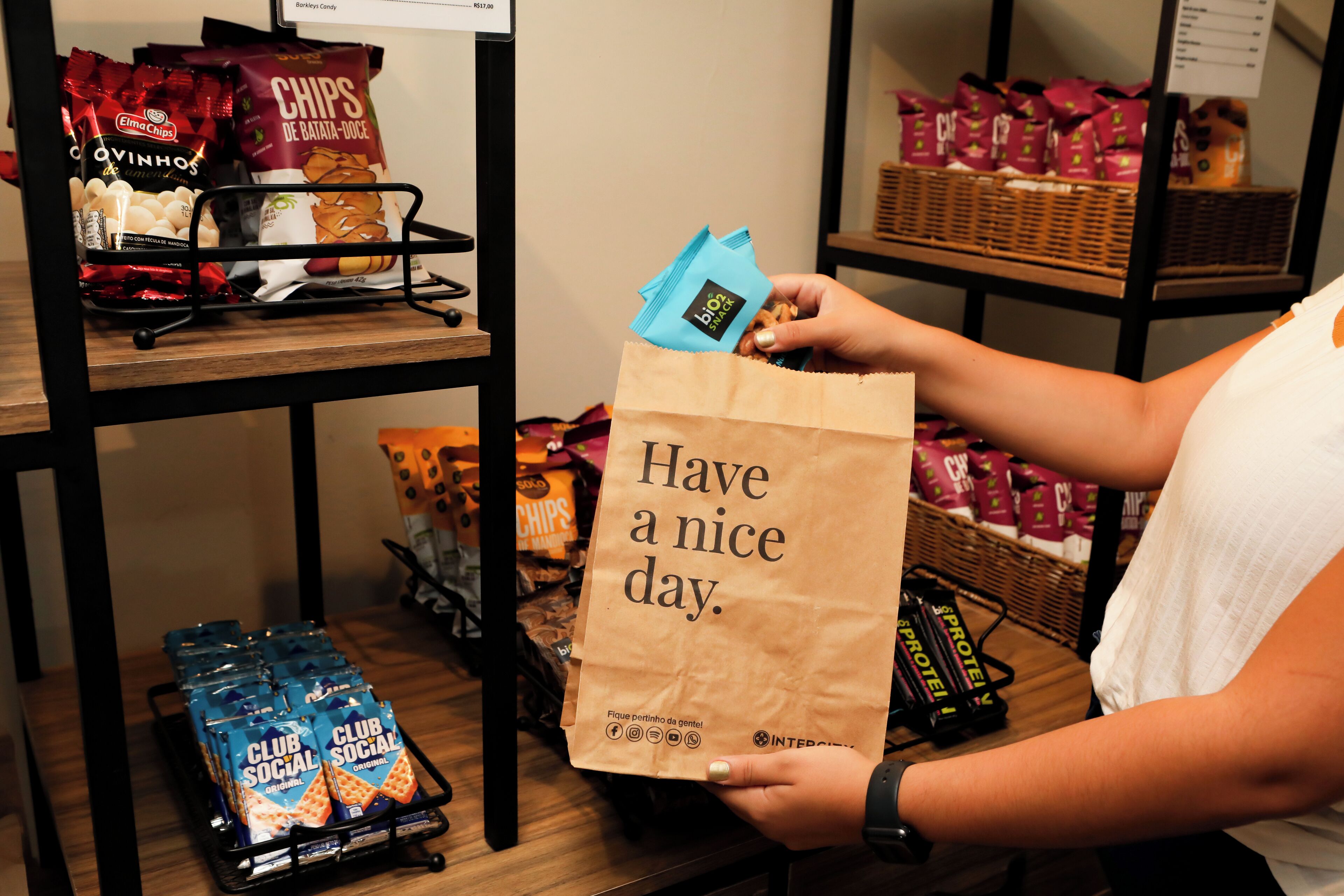 A person holding a paper bag with the text "Have a nice day." in a store with snack items on shelves.