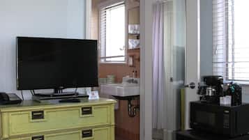 Quarto com cama, televisão, penteadeira, micro-ondas e banheiro visível por uma porta aberta.