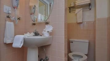 Un baño con lavamanos, espejo e inodoro. Hay toallas colgadas en la pared y un estante con más toallas.