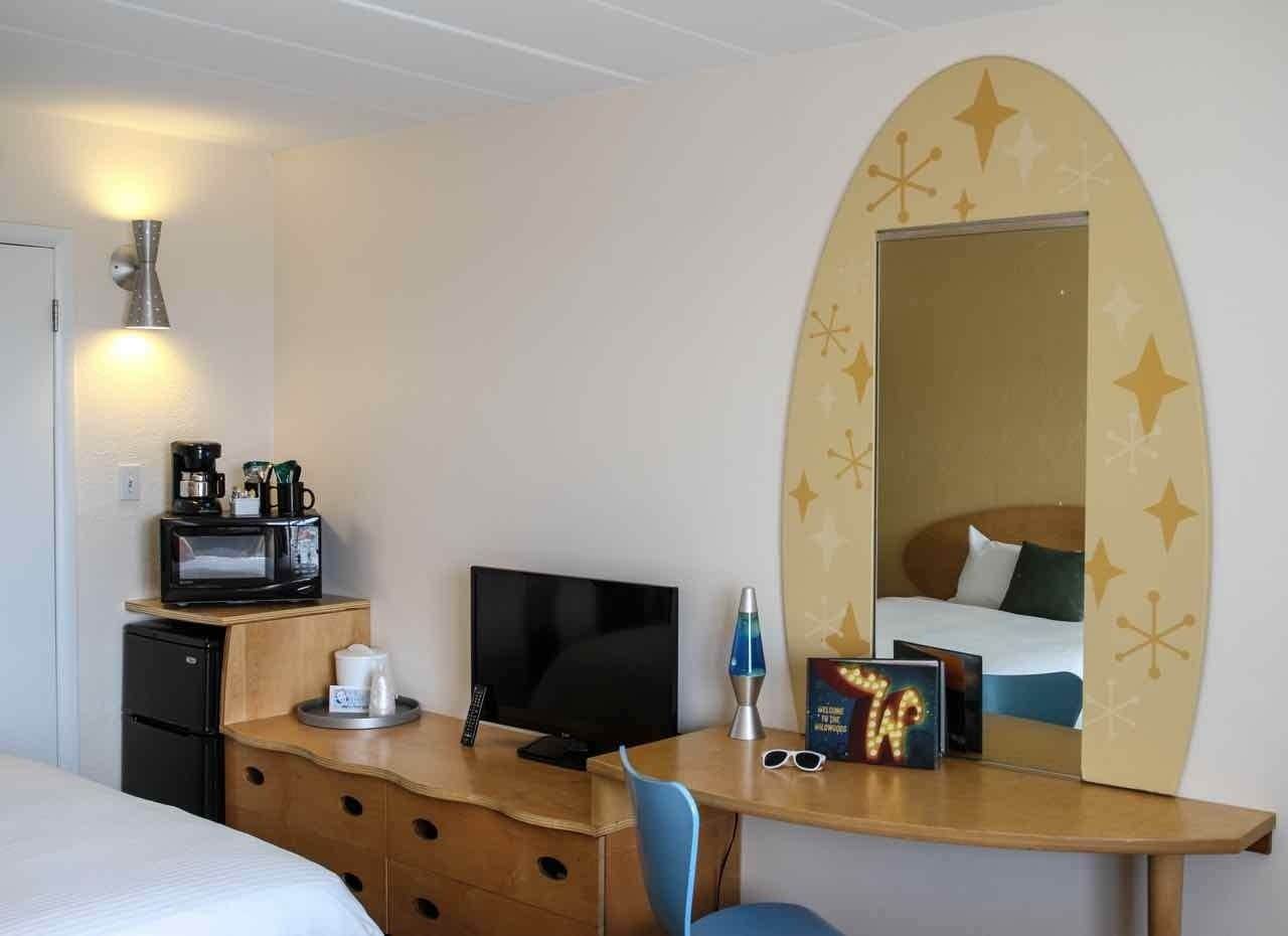 A hotel room with a bed, a desk with a television, a coffee maker, and a lava lamp.
