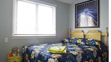 Un dormitorio con un ventanal grande, una cama con ropa de cama floral, un cuadro en la pared y un bolso pequeño en el suelo.