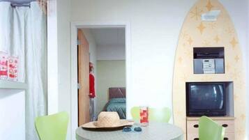 A room with a round table, green chairs, a television, and a decorative wall.