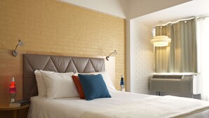 A neatly made bed with a quilted headboard, a bedside table with a lava lamp, and a window with curtains. - Starlux Hotel (Wildwood)