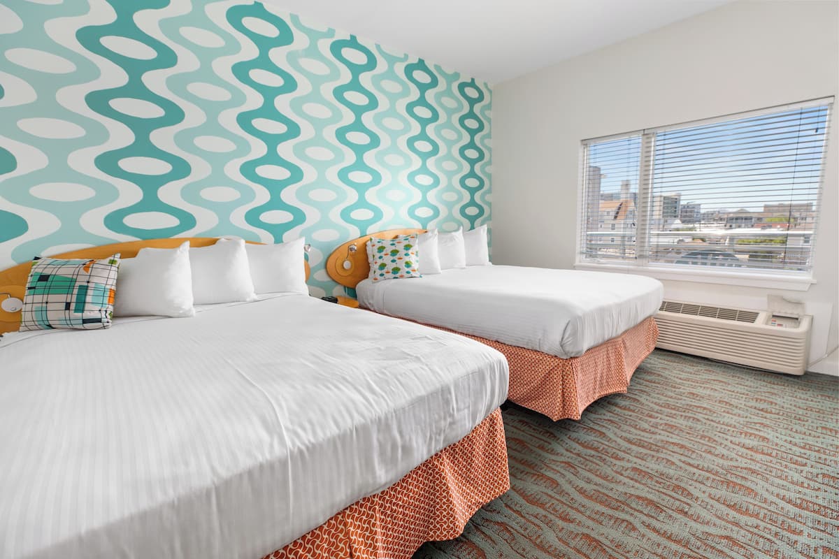 Quarto de hotel com duas camas, parede estampada, janela grande e chão coberto por carpete.