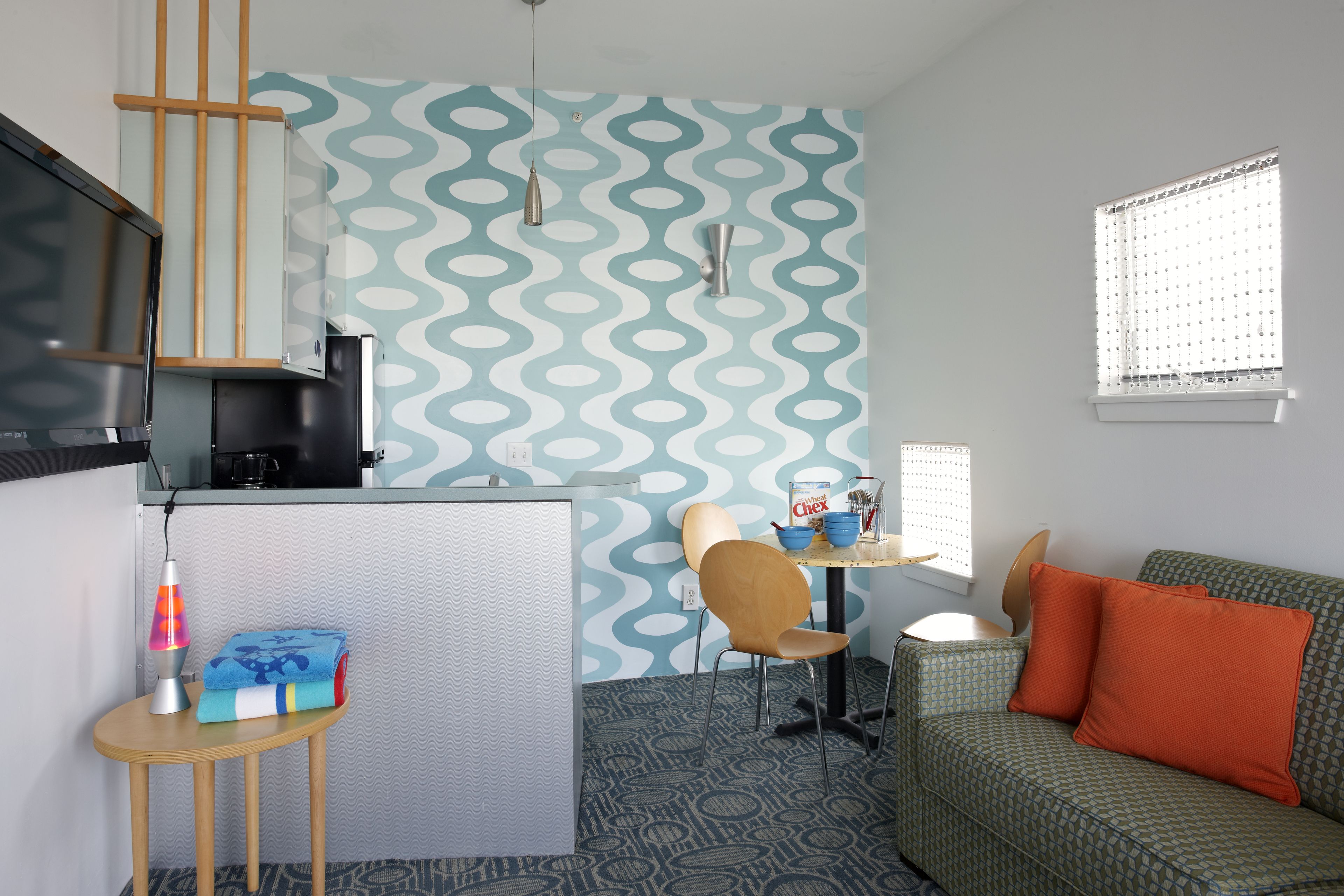 Un espacio habitable compacto con kitchenette, comedor y sofá con cojines naranjas.