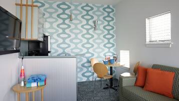 Un espacio habitable compacto con kitchenette, comedor y sofá con cojines naranjas.