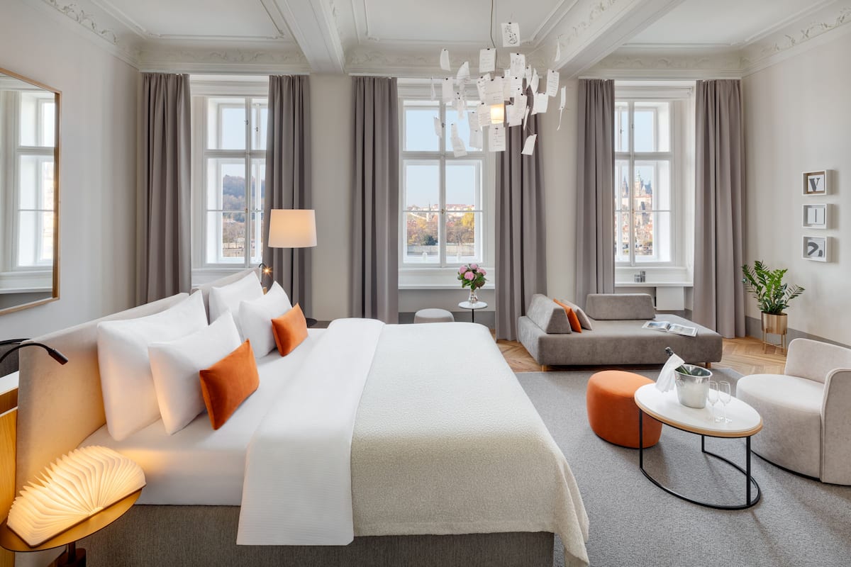 A modern hotel room with a large bed, a sofa, a small table, and a view of the city.