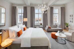 A modern hotel room with a large bed, a sofa, a small table, and a view of the city. - Boutique Hotel BOOKQUET (Prague)