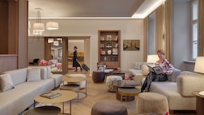 A spacious lounge area with a sofa, ottomans, and a coffee table. A bookshelf and a painting are visible on the wall. - Boutique Hotel BOOKQUET (Prague)