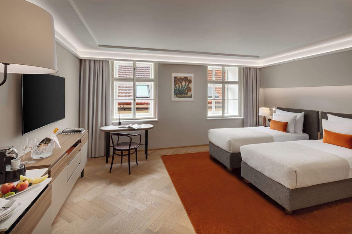 A hotel room with two beds, a desk with a chair, a TV, and a window with curtains.
