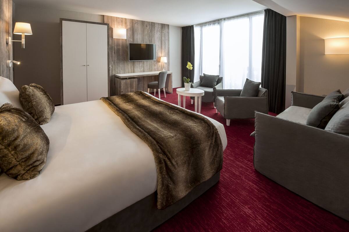 A hotel room with a large bed, a desk, a sofa, and a TV.