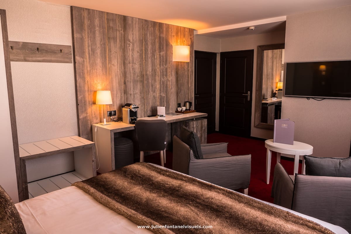 A hotel room with a bed, a desk, a chair, a TV, and a small table.