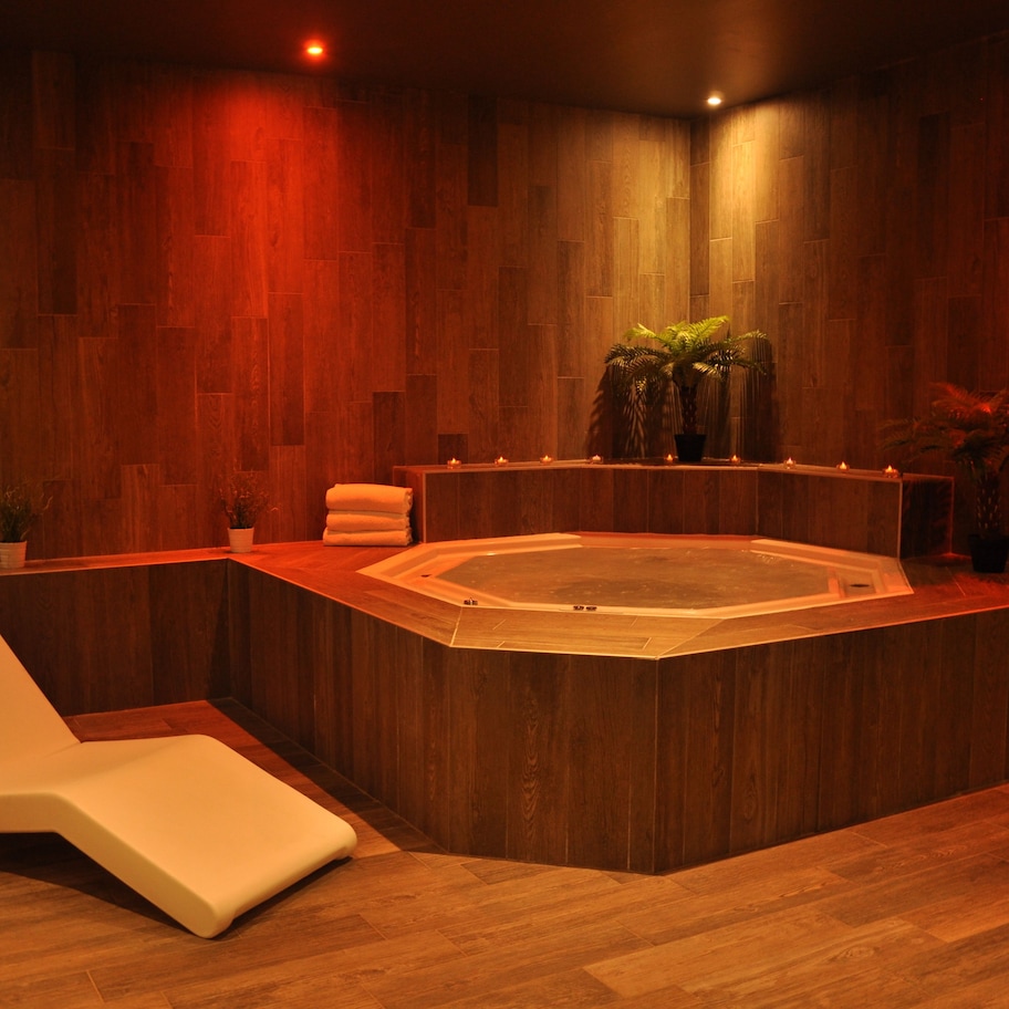 A spa room with a wooden floor, a hot tub, a white lounge chair, and potted plants.