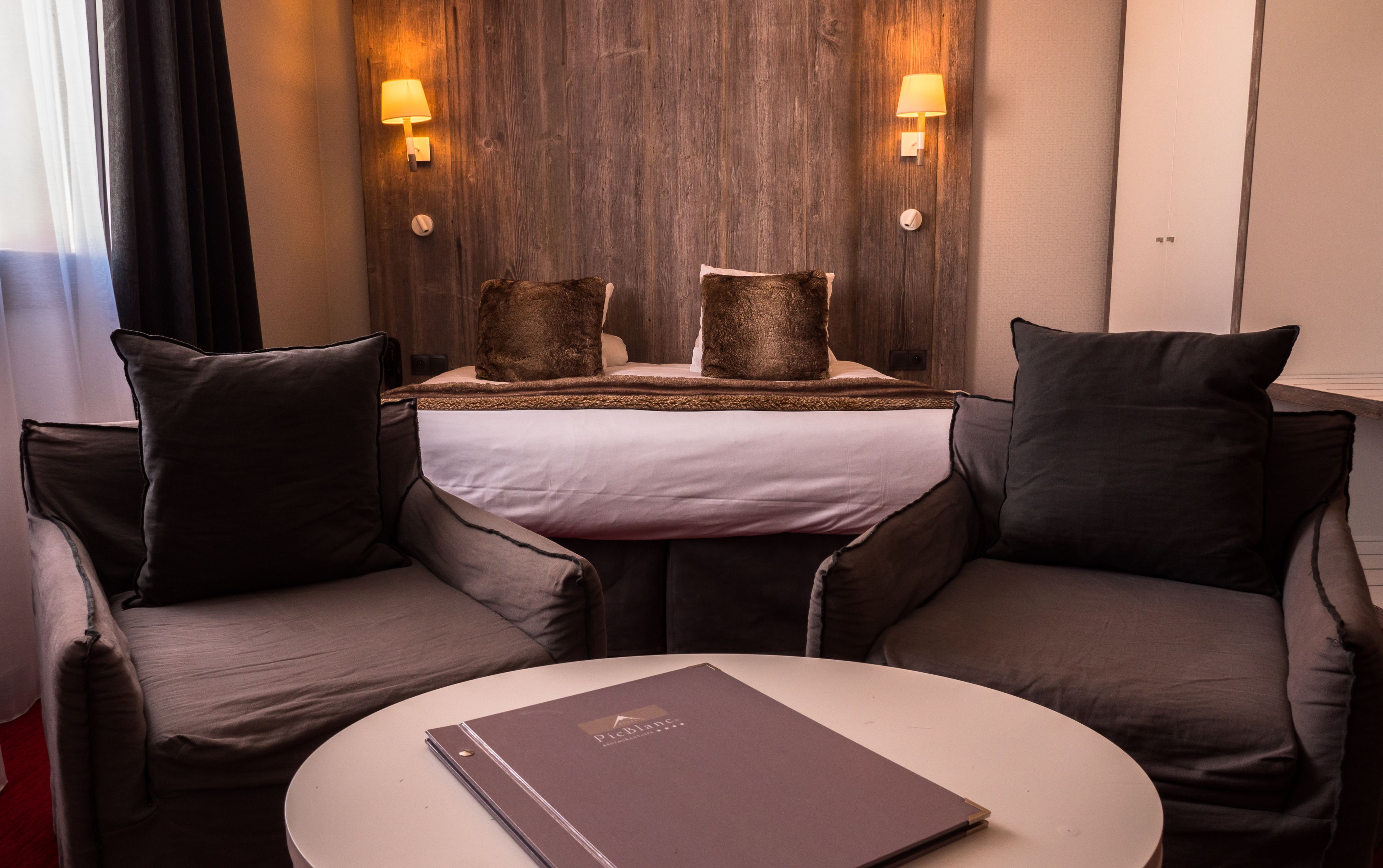 Une chambre d’hôtel comprenant un lit, deux lampes de chevet, une table de chevet, une table ronde avec un classeur et deux fauteuils.