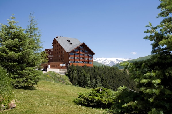 Ein Hotel mit einer auffälligen roten Fassade, mehreren Balkonen und Blick auf schneebedeckte Berge im Hintergrund.