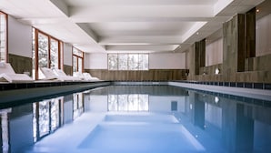 A large indoor swimming pool with clear water, surrounded by walls with large windows and a view of trees outside. - Hôtel Le Pic Blanc (Huez)