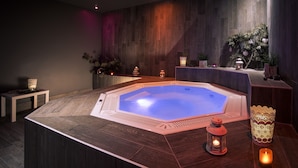 A modern spa room with a central heated pool, wooden flooring, and ambient lighting. - Hôtel Le Pic Blanc (Huez)