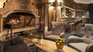 A cozy lounge area with a fireplace, comfortable seating, and a bar with a rustic wooden backdrop. - Hôtel Le Pic Blanc (Huez)