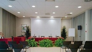 A conference room with a red table, chairs, a projector screen, and a whiteboard. - JR Hotels Gigli Firenze (Calenzano)