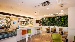 Zona de bar con diversas opciones de asientos, una barra con selección de botellas y una pared verde con plantas.