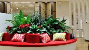 Un sofá rojo con cojines estampados, rodeado de grandes plantas verdes y flores rojas.
