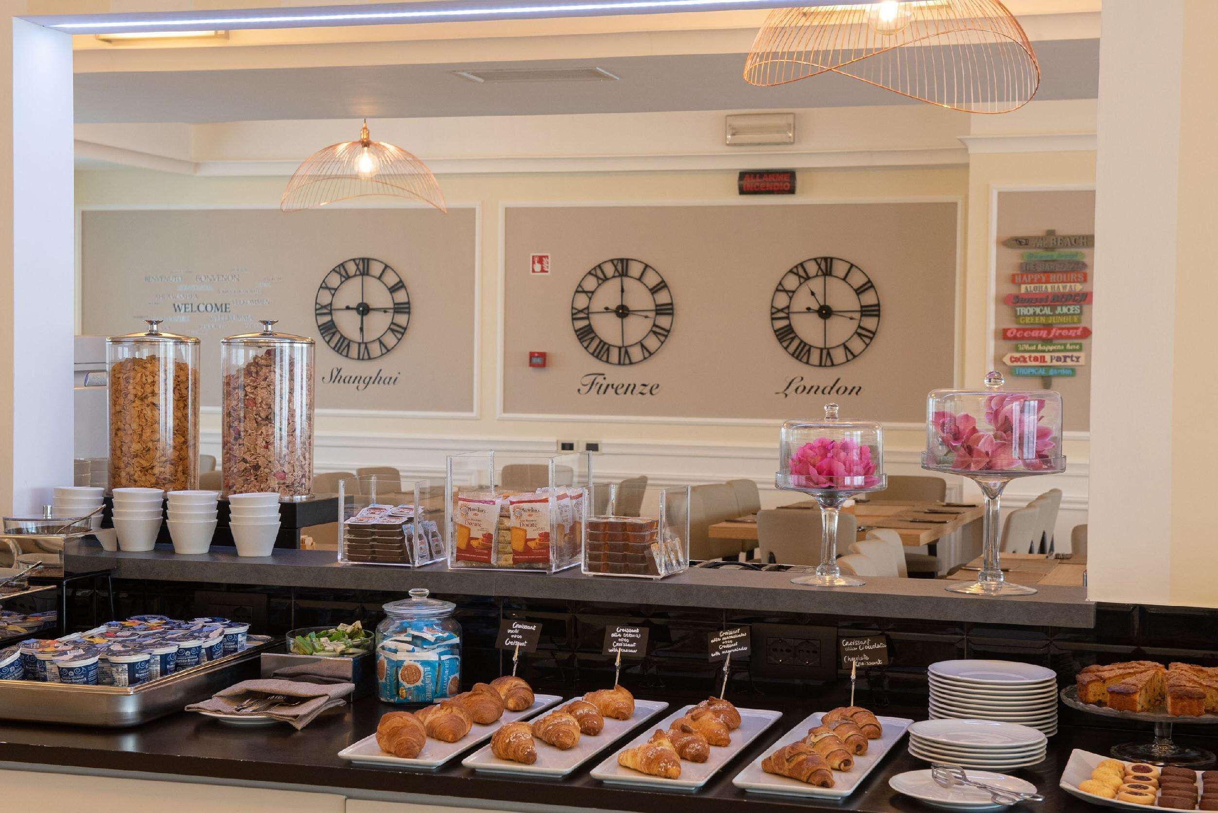 A buffet counter with various food items, including pastries and condiments, and clocks indicating different cities.