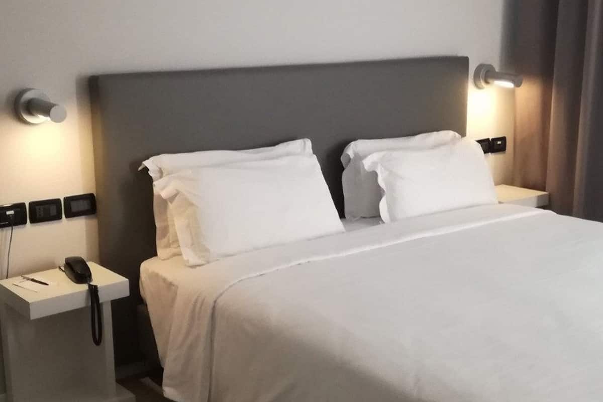 A neatly made bed with white linens in a modern hotel room.