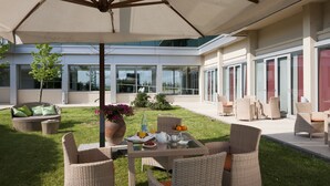 Un espacio moderno para comer al aire libre con mobiliario de mimbre, una mesa servida con desayuno y una gran sombrilla que da sombra.