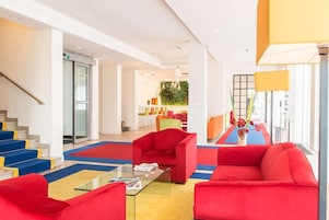 Un vestíbulo moderno con sofás rojos, una mesa de centro de vidrio y una escalera con detalles azules y amarillos.