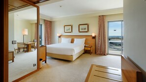 Habitación de hotel con una cama grande, un escritorio, una silla, una mesita, un espejo y ventana con vistas al aeropuerto.