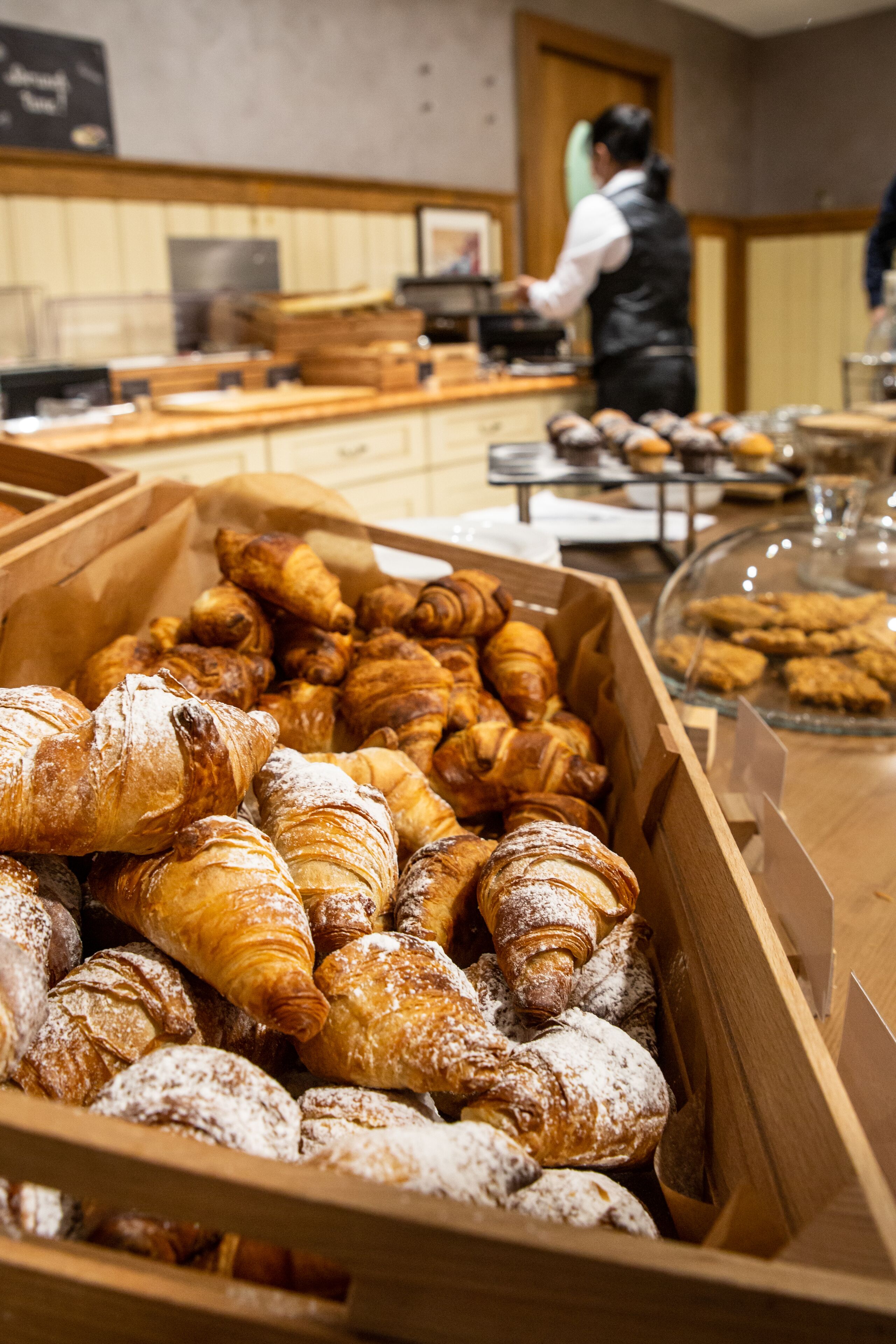 A bakery display with various pastries and a person in the background.