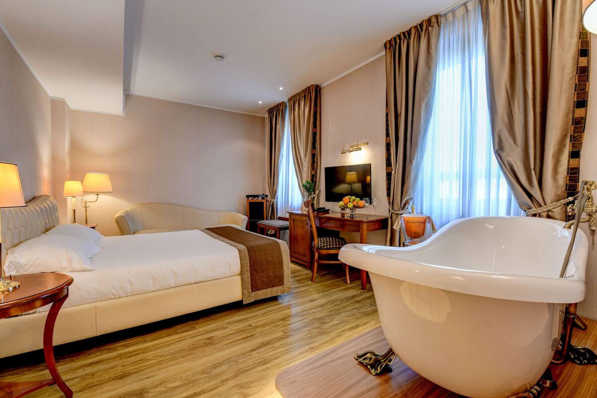 A hotel room with a large bed, a sitting area with a desk and chair, a bathtub, and a television.