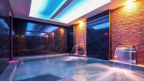 Un área de piscina interior moderna con techo de cristal, pared de ladrillo y suelo de mármol.