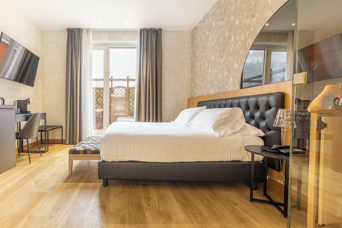 A modern hotel room with a large bed, a desk, and a glass partition.