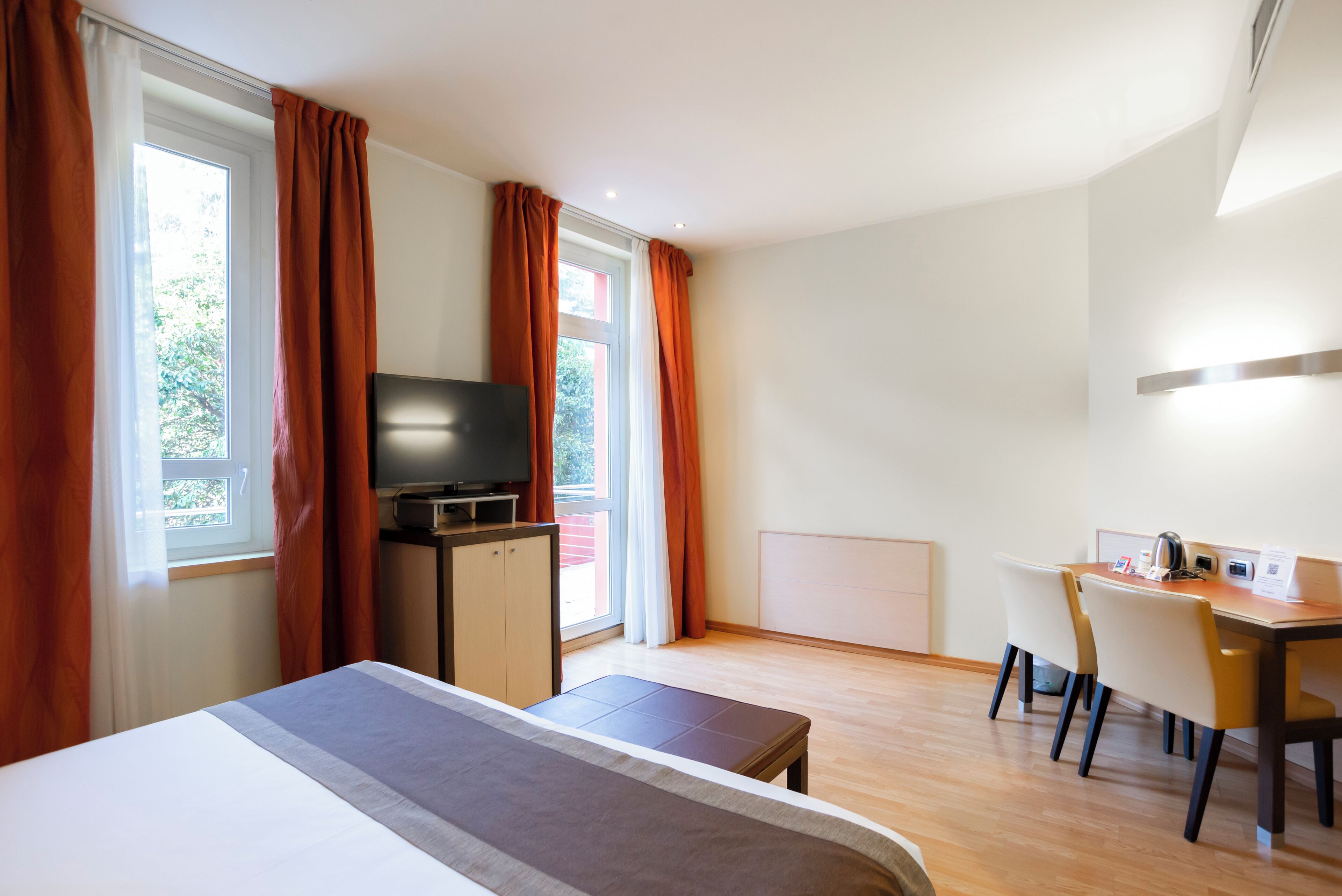 Een hotelkamer met een bed, een bureau, een stoel, een televisie en een raam met gordijnen.