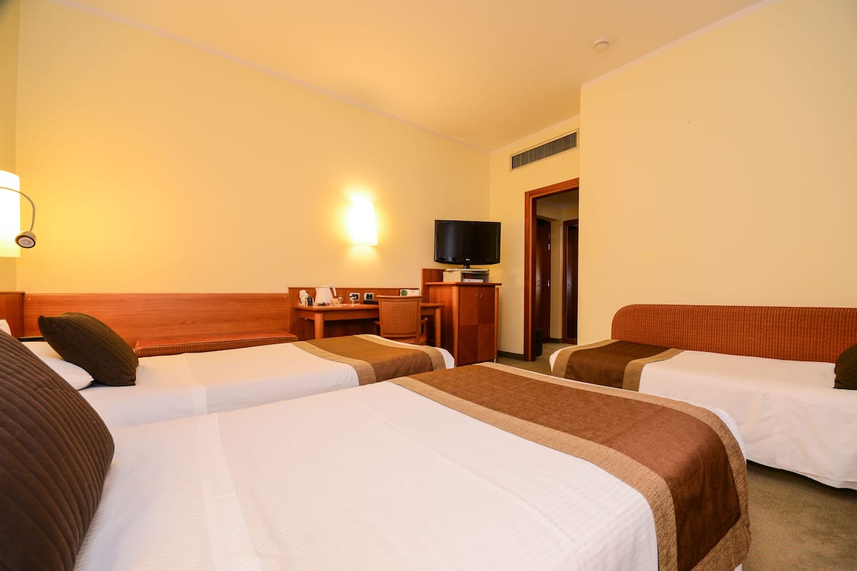 A hotel room with two beds, a desk, a chair, a television, and a lamp.